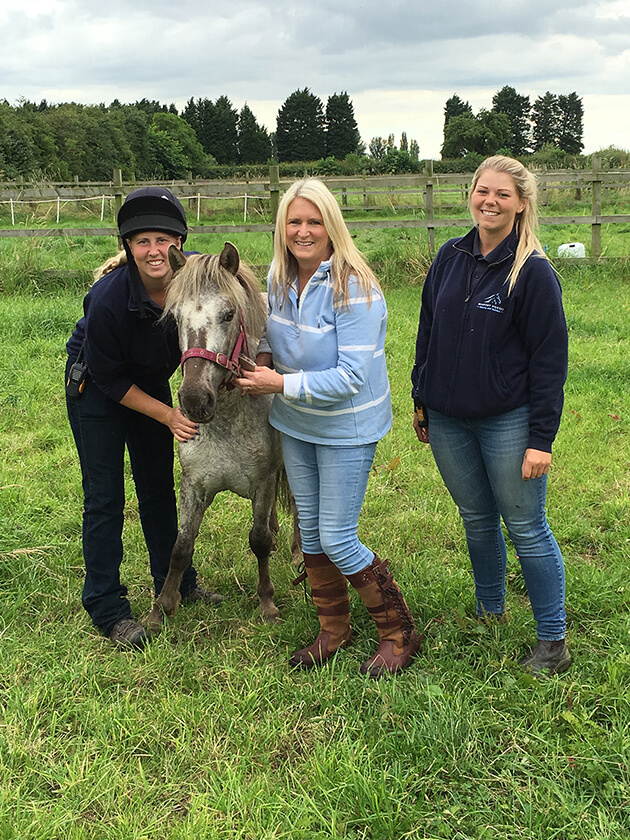 members of staff and a woman stood next to a dappled grey pony in a field