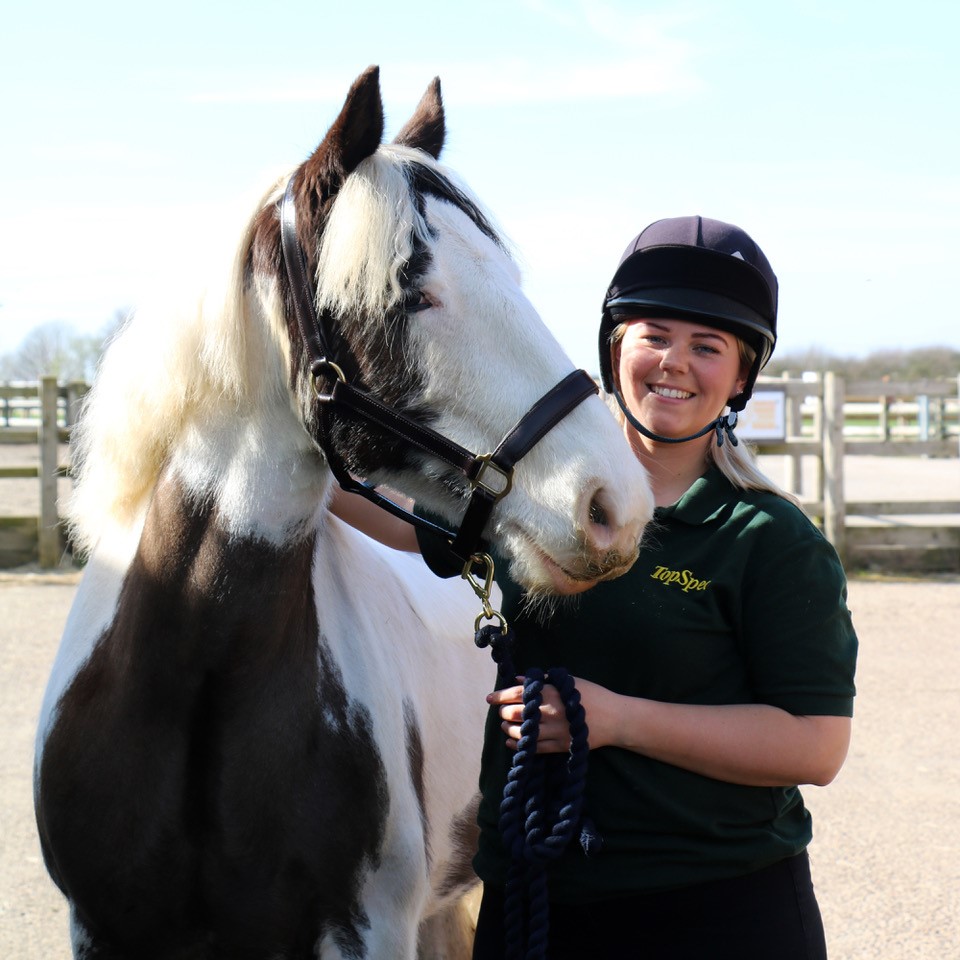 woman wearing a helmet stood next to a black and white cob wearing a black headcollar