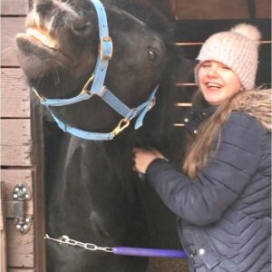 black pony with a young girl stood in a stable