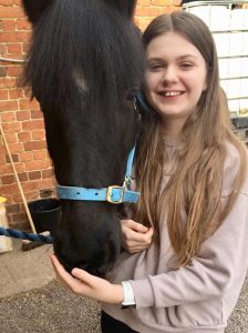 young girl stood next to a black pony wearing a blue headcollar