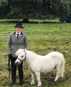 woman stood next to a grey shetland pony in a field