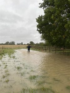 Member of staff stood in a flooded field demonstrating how deep the water is