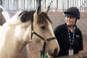 member of staff leading a tan and white horse around an indoor arena
