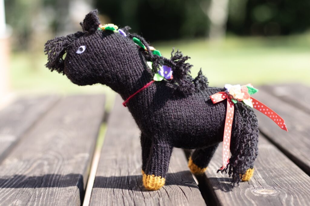 black hand knitted pony with gold hooves and flowers in its mane