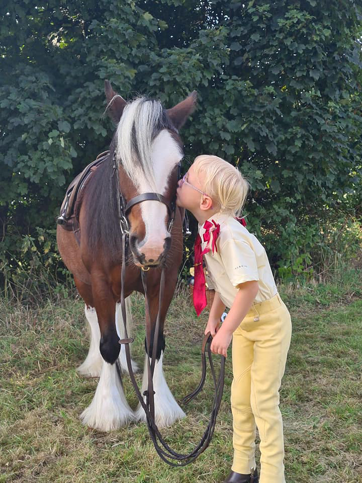 Young girl kissing the face of a tacked up skewbald pony