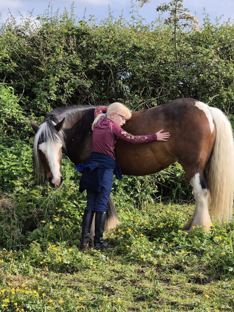 Young girl stood to the side of a skewbald pony