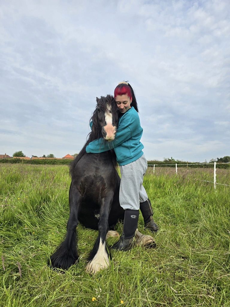 Black cob sat down in a field with his fosterer cuddling him