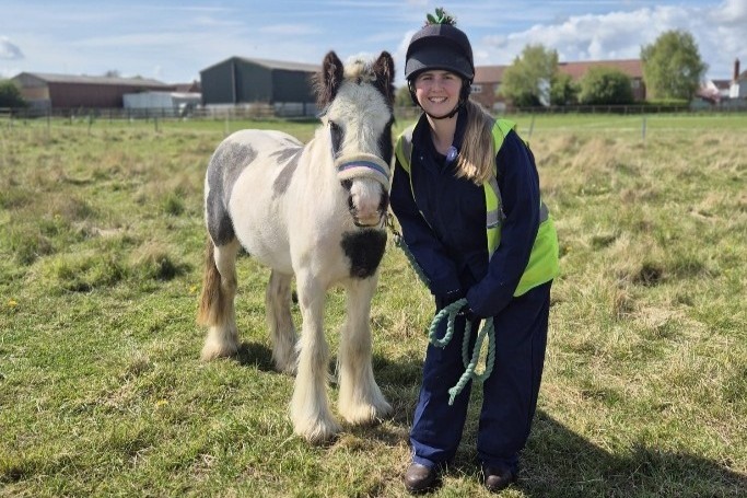 a member of staff stood next to a small black and white cob in a field