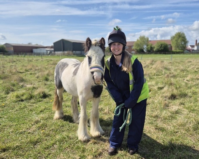a member of staff stood next to a small black and white cob in a field