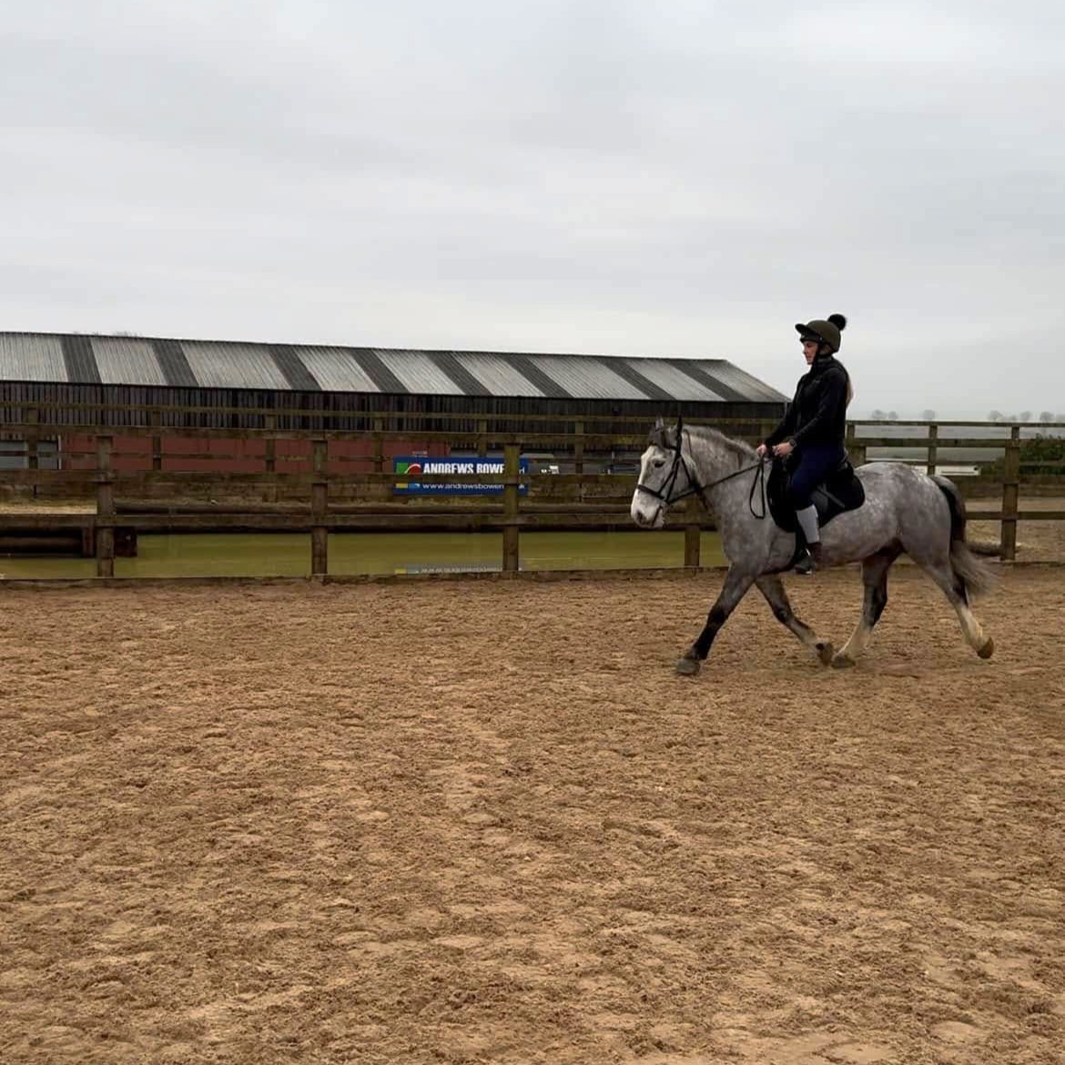 A woman riding a grey dappled pony in a menage