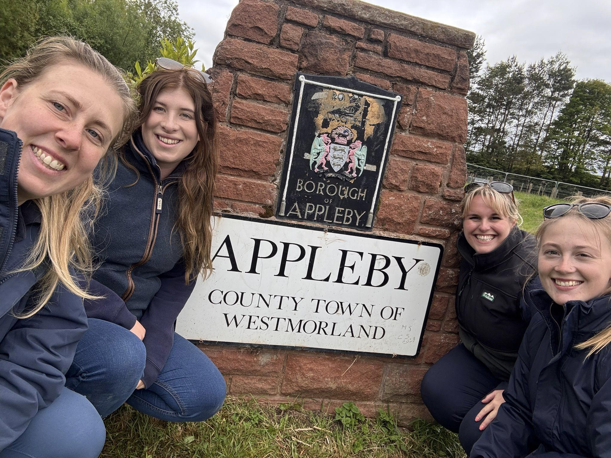 Four Bransby Horses staff members pose beside a stone “Borough of Appleby” sign, smiling at the camera while attending Appleby Fair.